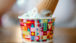 Ice cream cone with white soft-serve frozen yogurt in a colorful geometric patterned paper cup.