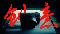 Rangefinder camera on textured surface with bold red typography overlaid on either side.