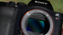 Sony α7R mirrorless camera with E-mount lens mount exposed, showing sensor and internal mechanics against blurred green background.