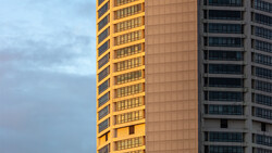 Two residential high-rise buildings with contrasting facades during golden hour, one illuminated in warm yellow tones and one in cool gray tones.