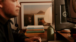 Desk setup with stacked books, desk lamp, and monitor displaying interior photographs.