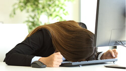 Person in black blazer slumped over desk with head resting on keyboard.