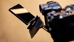A reflective white and black photography reference card held in front of a camera against a warm beige background.