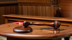 Wooden gavel and sound block on a polished round table in a courtroom setting.
