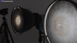 Two studio light fixtures with reflectors positioned against a dark gray background, one with visible dome reflector and one with honeycomb grid.
