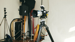 Photography studio setup with tripod-mounted telescope lens, lighting equipment, and camera gear on wooden floor.