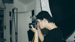 Photographer operating a camera mounted on a tripod with studio lighting setup in an indoor space.