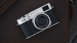 Rangefinder camera with silver top plate and black leather body on a dark textured surface.