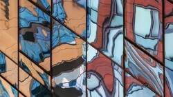 Reflections of blue sky and building facades in glass windows of a modern building.