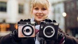 Child holding two vintage instant film cameras with black and beige bodies in an urban outdoor setting.