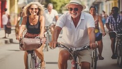 Couple riding bicycles down a sunny street lined with pedestrians and colorful buildings.