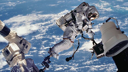 Astronaut performing a spacewalk with Earth and clouds visible in the background.