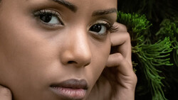 Close-up portrait of a woman with hand to face, looking at camera with serious expression.