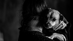Person holding a small dog over their shoulder in a high-contrast black and white portrait.