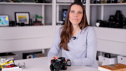 Woman presenter demonstrating a professional DSLR camera at a desk in a studio setting.