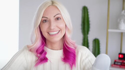 Portrait of a woman with platinum blonde and magenta ombre hair smiling at camera in studio setting.