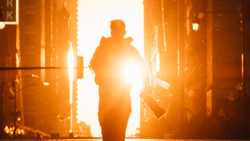 Silhouetted figure walking toward bright golden light between urban buildings at sunset.