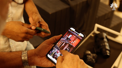 Person holding smartphone displaying photo gallery app with warm indoor lighting and blurred background.