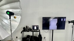 Professional photography studio setup with white umbrella reflector, monitor, and multiple studio lights on stands.
