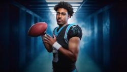 Football player in Panthers uniform holding a football in an illuminated corridor.