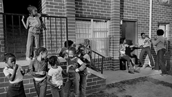 Children playing in an urban alley beside a brick building in this black and white street photograph.