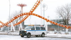 White and blue van parked in front of an orange roller coaster structure in an amusement park setting.