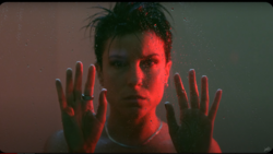 Person with hands pressed against glass, face lit by red and green theatrical lighting.