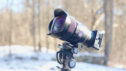 Wide-angle lens mounted on ball head tripod with winter forest background.