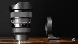Wide-angle lens with lens hood and tripod collar mounted on wooden surface against black background.