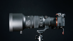 Professional camera lens mounted on tripod head with focus and zoom rings visible against dark background.