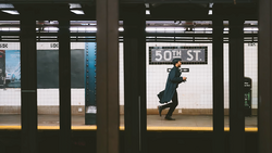 Man in dark coat running through subway station past 50th Street platform sign.