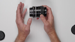 Hands holding a vintage camera lens with focus and aperture rings against a white background.