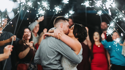Couple kissing while guests hold sparklers around them at night.