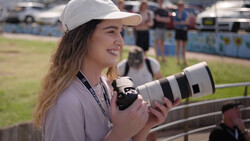 Female photographer holding a telephoto lens at an outdoor sports event.