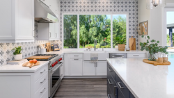 Modern kitchen with white cabinetry, stainless steel appliances, and patterned backsplash overlooking trees through large windows.