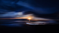 Sunset over ocean horizon with motion blur effect and dramatic cloud formations.