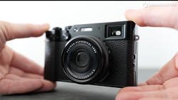 Hands holding a black rangefinder-style digital camera with textured grip and fixed lens.