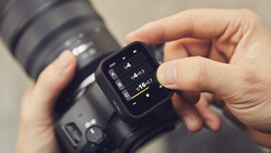 Photographer's hands holding a camera with an external wireless remote trigger displaying exposure settings.