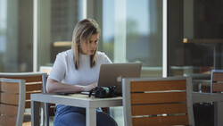 Woman working on laptop at outdoor table with city skyline in background.
