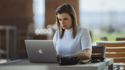 Woman working on MacBook at outdoor table with camera equipment nearby.