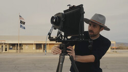 Photographer holding a large format camera on a tripod in an empty parking lot.