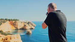Photographer shooting a coastal landscape with dramatic rocky cliffs and turquoise water.