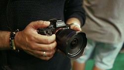 Photographer's hands holding a Sony mirrorless camera with wide-angle lens attached.