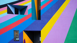 Colorful geometric mural with diagonal stripes in blue, pink, yellow, purple, and green, featuring black architectural elements and doorways.