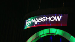 Illuminated NAB Show signage with curved green and red neon lighting against dark background.