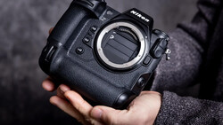 Nikon professional camera body held in hands, showing the lens mount and control buttons against a dark textured background.