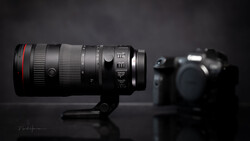 Professional telephoto lens with red ring mounted on stand, camera body blurred in background.