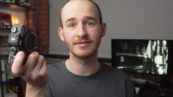 Filmmaker holding a vintage Super 8 camera toward the viewer in a studio setting.