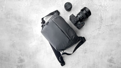 Flat lay of camera gear including DSLR body with attached lens, shoulder bag, and lens cap on concrete surface.
