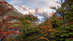 Snow-capped mountain peak framed by autumn foliage in a valley landscape.